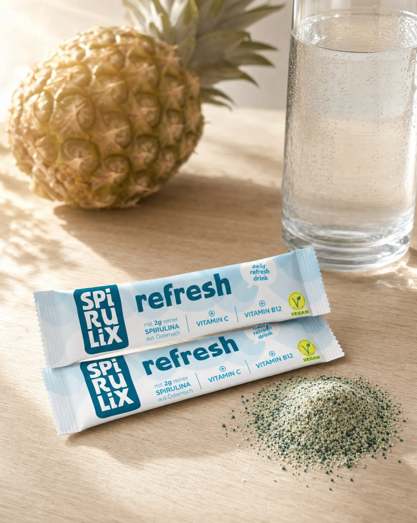 Two SPIRULIX Refresh sticks on an oak table with pineapple, water and a mound of drink powder